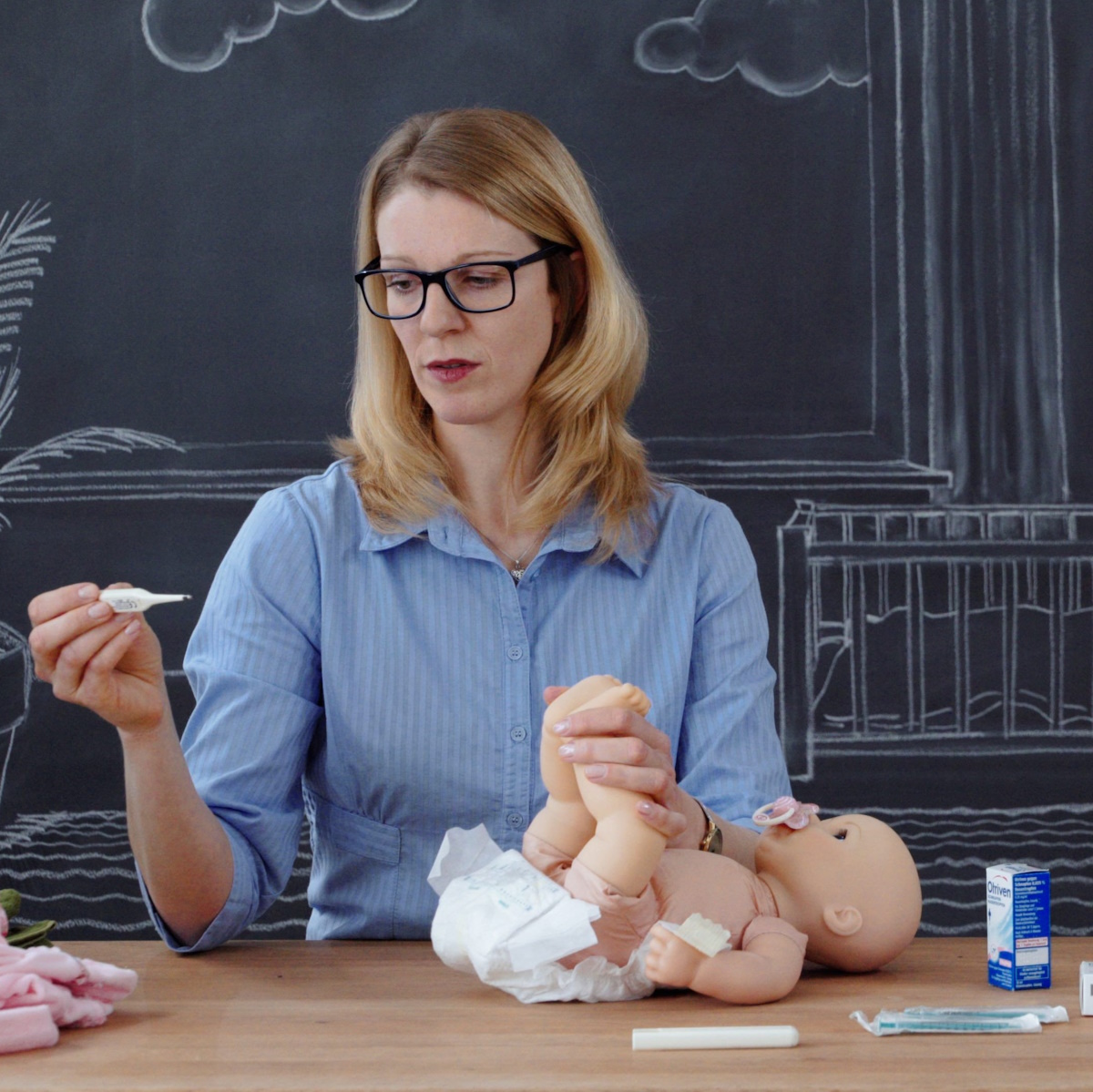 &Auml;rztin demonstriert an Puppe, wie Fiebermessen beim Baby geht