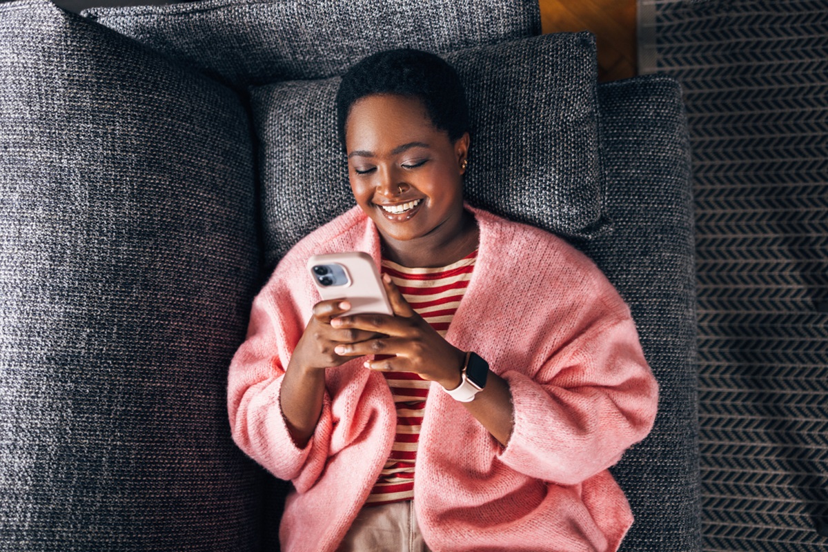 Handysucht, Frau schaut ins Smartphone auf der Couch liegend