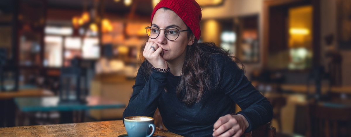 Eine junge Frau sitzt alleine am Tisch, ihr Smartphone liegt vor ihr.