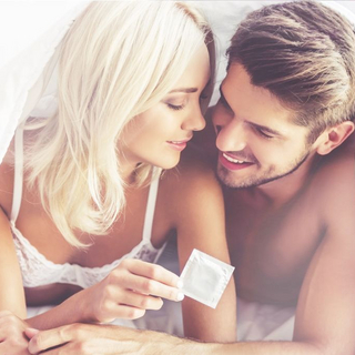 Paar liegt im Bett und h&auml;lt ein Kondom in der Hand