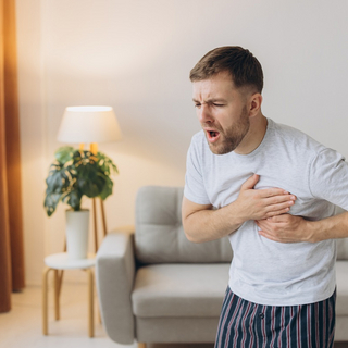 Ein junger Mann h&auml;lt sich die Hand ans Herz, hat ein schmerzverzehrtes Gesicht wegen einer Panikattacke.