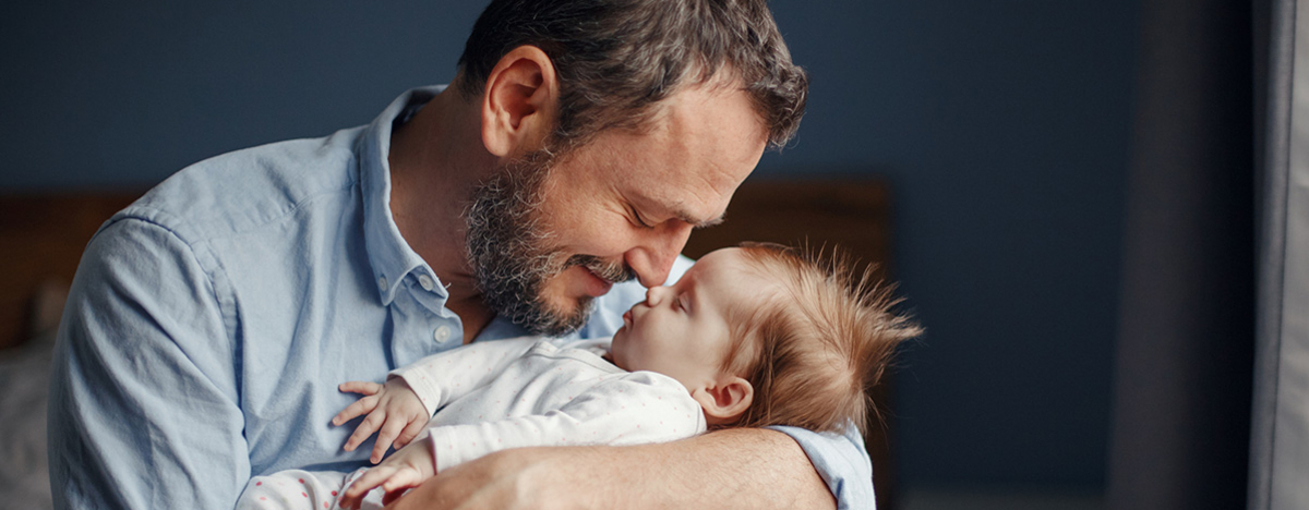 Vater im mittleren Alter k&uuml;sst schlafendes neugeborenes M&auml;dchen