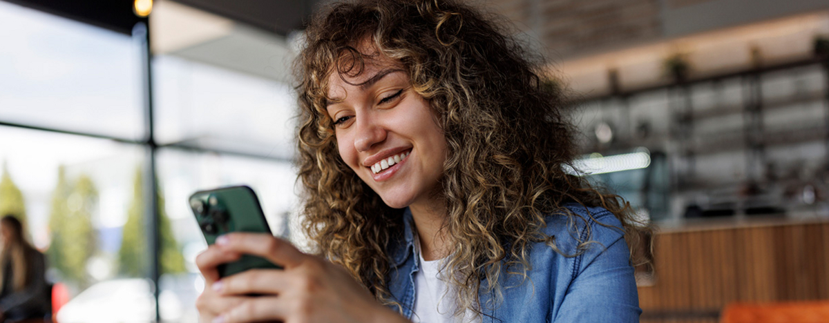 Junge l&auml;chelnde Frau mit Handy in der Hand