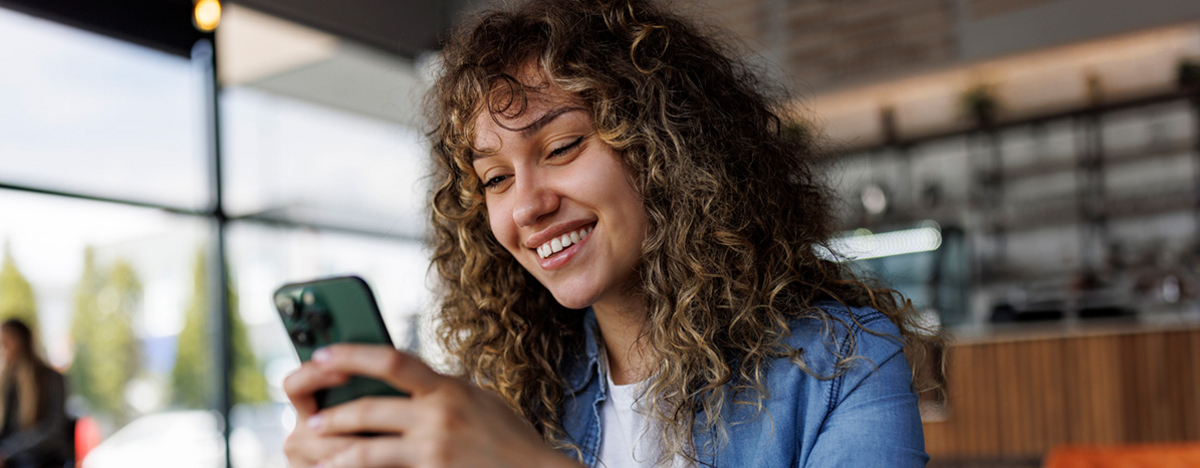 Junge l&auml;chelnde Frau mit Handy in der Hand