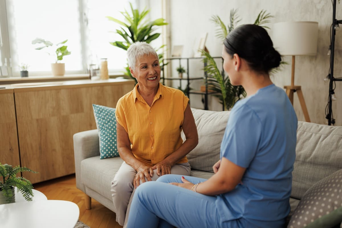 Seniorin unterh&auml;lt sich nett mit einer Krankenschwester zu Hause.