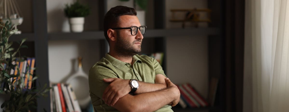 Overthinking: Ein Mann sitzt auf einem Stuhl und schaut nachdenklich aus dem Fenster.