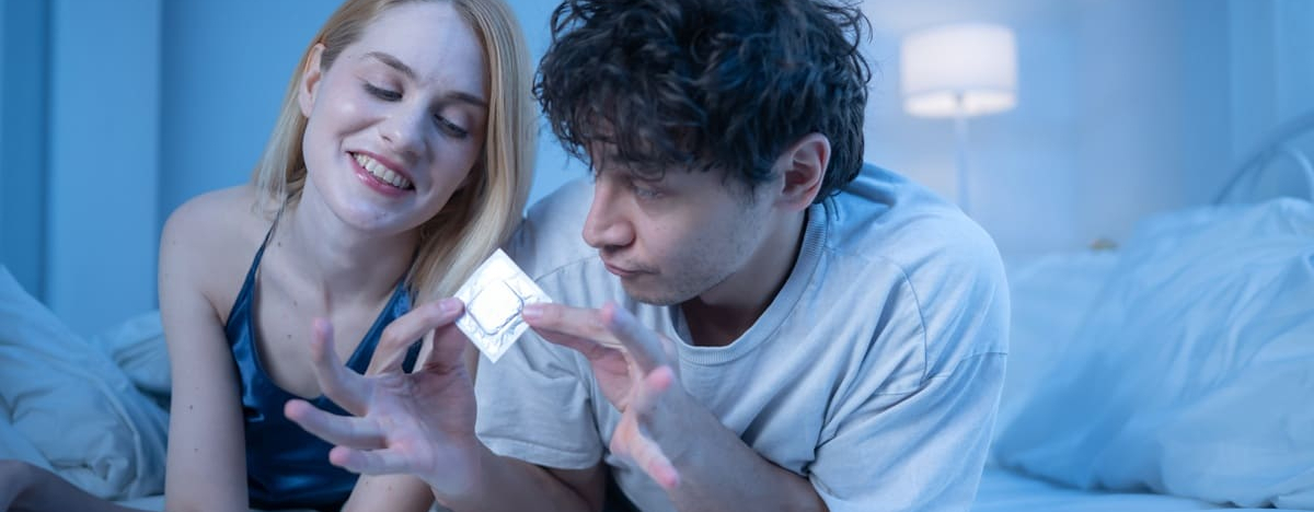 Junges Paar im Bett mit Kondom in der Hand, das Intimit&auml;t, Romantik und Safer Sex zeigt