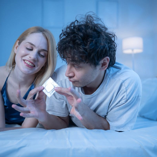 Junges Paar im Bett mit Kondom in der Hand, das Intimit&auml;t, Romantik und Safer Sex zeigt