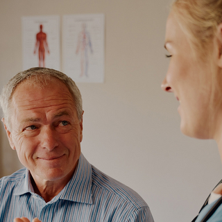 Gl&uuml;cklicher pensionierter Patient sitzt in Klinik und h&ouml;rt &Auml;rztin &uuml;ber Behandlung zu