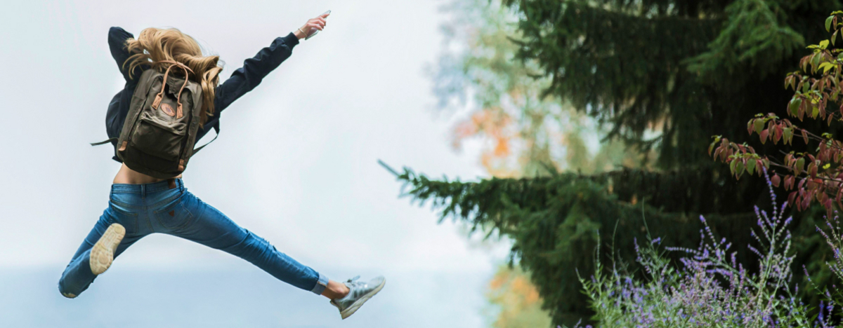 Eine Junge Frau mit Rucksack springt fr&ouml;hlich durch den Wald.
