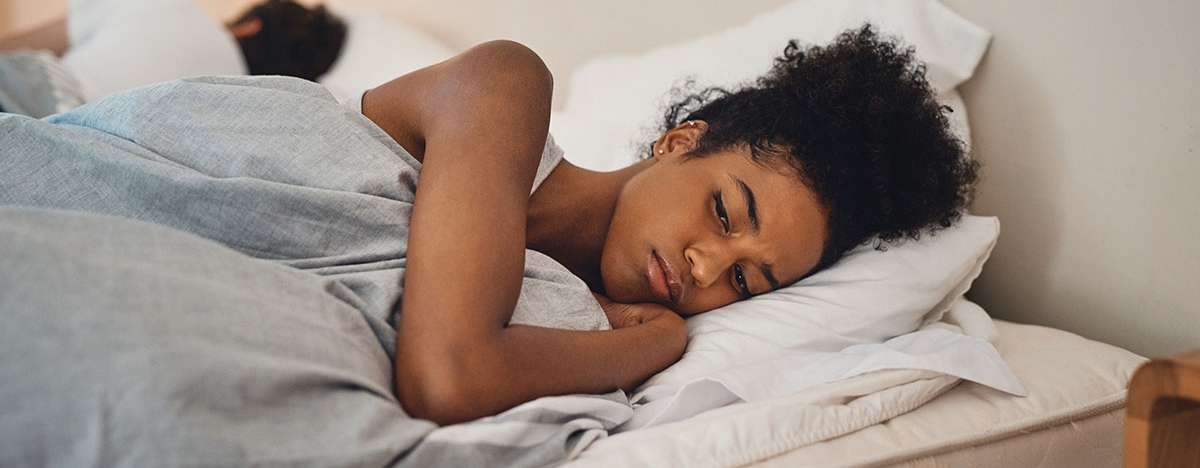 Frau liegt wach neben Mann im Bett