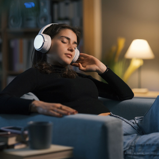 Frau sitzt entspannt im Sessel und h&ouml;rt &uuml;ber Kopfh&ouml;rer Musik