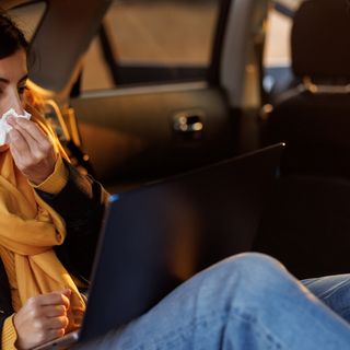 Frau sitzt mit Taschentuch auf der R&uuml;ckbank im Auto