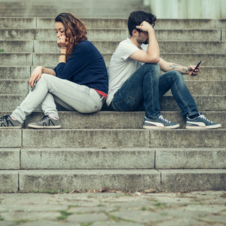 Eine Frau und ein Mann sitzen R&uuml;cken an R&uuml;cken auf einer Treppe und beachten sich nicht.