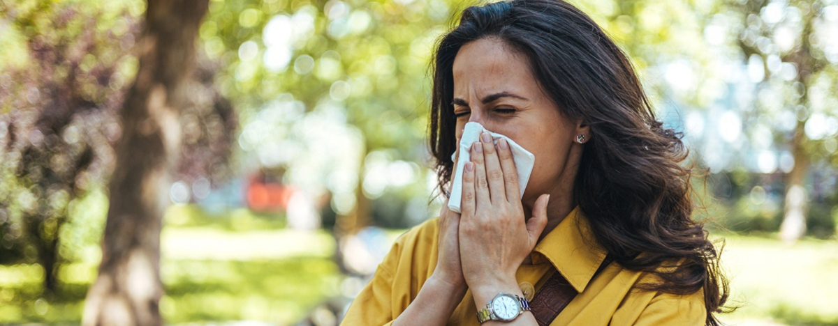 Eine Frau spaziert im Park, niest in ein Taschentuch wegen ihrer Allergie.