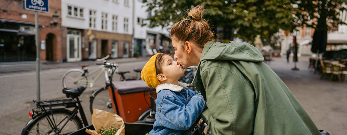 Mutter und Sohn geben sich ein K&uuml;sschen, w&auml;hrend sie bei einem Fahrradst&auml;nder stehen