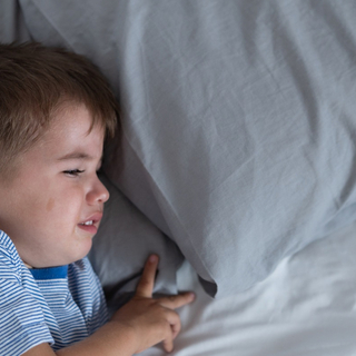 Kleiner Junge liegt in Bett, quengelt und schl&auml;ft nicht.