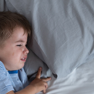 Kleiner Junge liegt in Bett, quengelt und schl&auml;ft nicht.