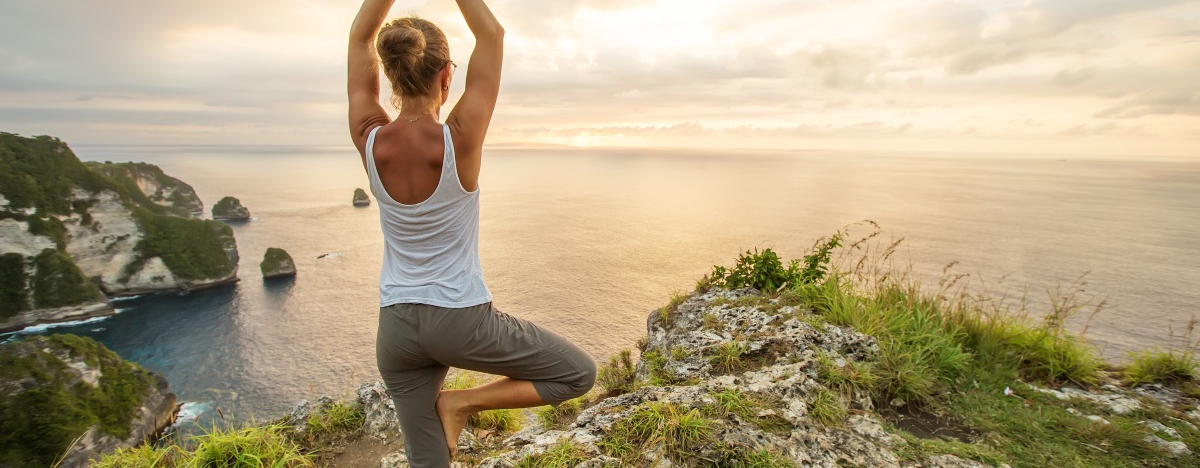 Frau steht auf einer Klippe und macht eine Yoga-&Uuml;bung