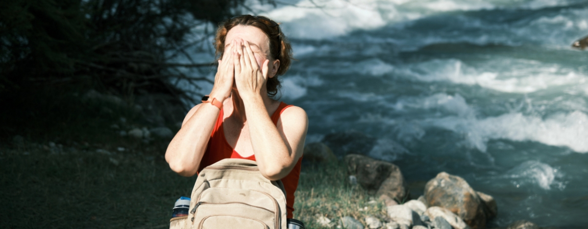 Frau steht in der Sonne an einem Fluss und h&auml;lt ihre H&auml;nde &uuml;ber das Gesicht