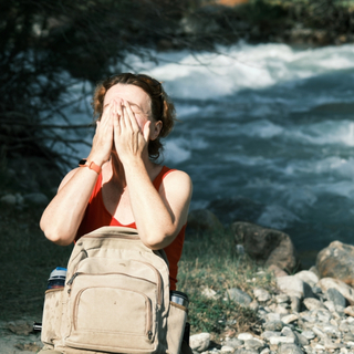 Frau steht in der Sonne an einem Fluss und h&auml;lt ihre H&auml;nde &uuml;ber das Gesicht