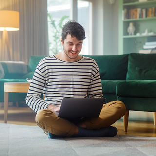 Mann mit Laptop, w&auml;hrend er auf dem Wohnzimmerboden sitzt