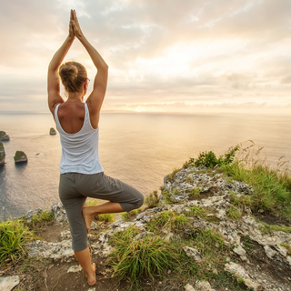 Frau steht auf einer Klippe und macht eine Yoga-&Uuml;bung