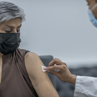 Eine &auml;ltere Dame mit Maske, die sich vom Arzt impfen l&auml;sst.