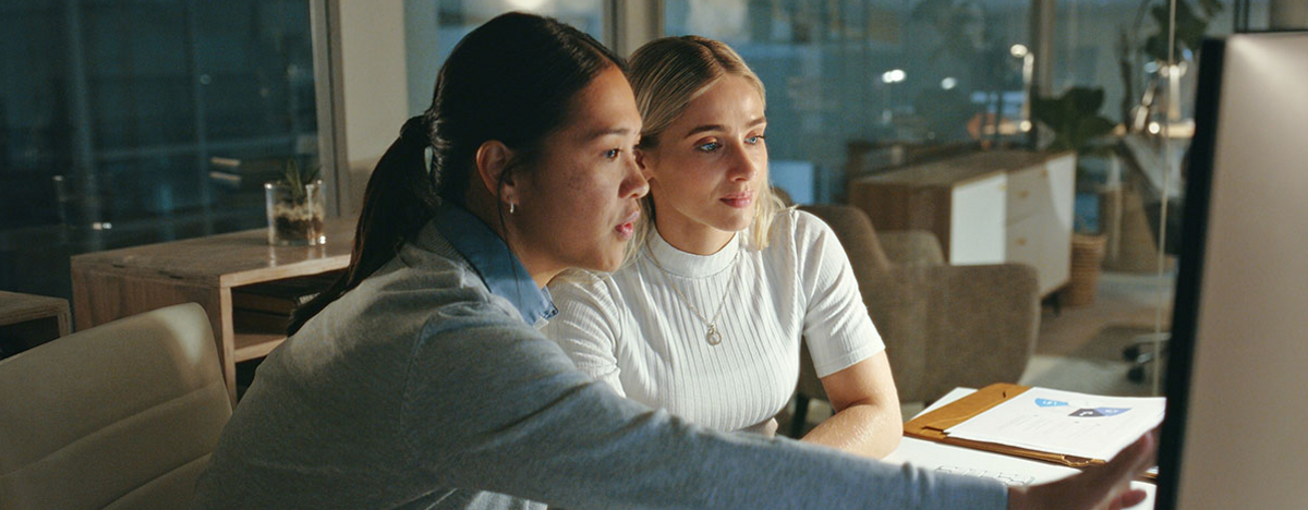Zwei Frauen, die zusammen &uuml;ber ein Projekt vor einem Computer sprechen
