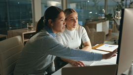 Zwei Frauen, die zusammen &uuml;ber ein Projekt vor einem Computer sprechen