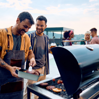 Zwei M&auml;nner stehen am Grill und lachen