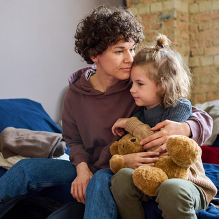 Junge Frau, die ihren kleinen Sohn mit braunem, weichem Teddyb&auml;ren umarmt