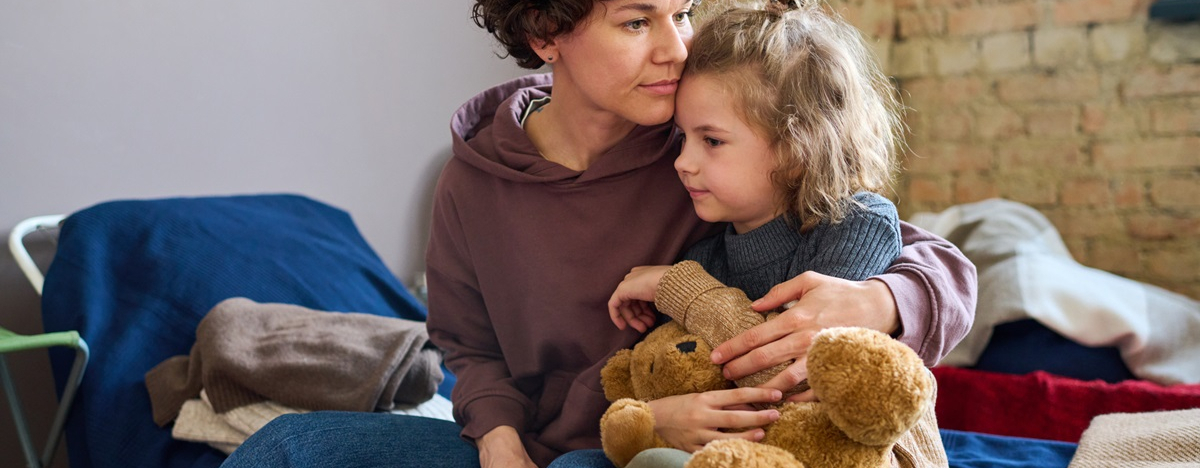 Junge Frau, die ihren kleinen Sohn mit braunem, weichem Teddyb&auml;ren umarmt