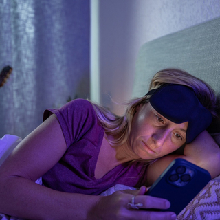 Eine Frau mittleren Alters liegt im Bett wegen Schlafproblemen und schaut auf ihr Smartphone
