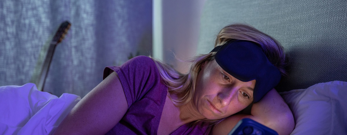 Eine Frau mittleren Alters liegt im Bett wegen Schlafproblemen und schaut auf ihr Smartphone