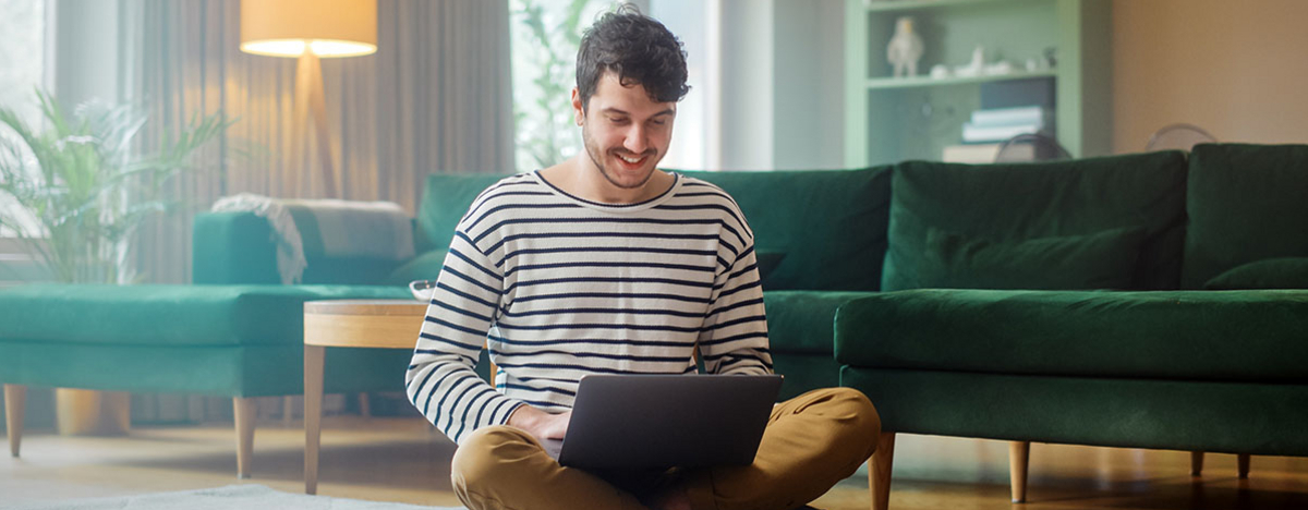 Mann mit Laptop, w&auml;hrend er auf dem Wohnzimmerboden sitzt
