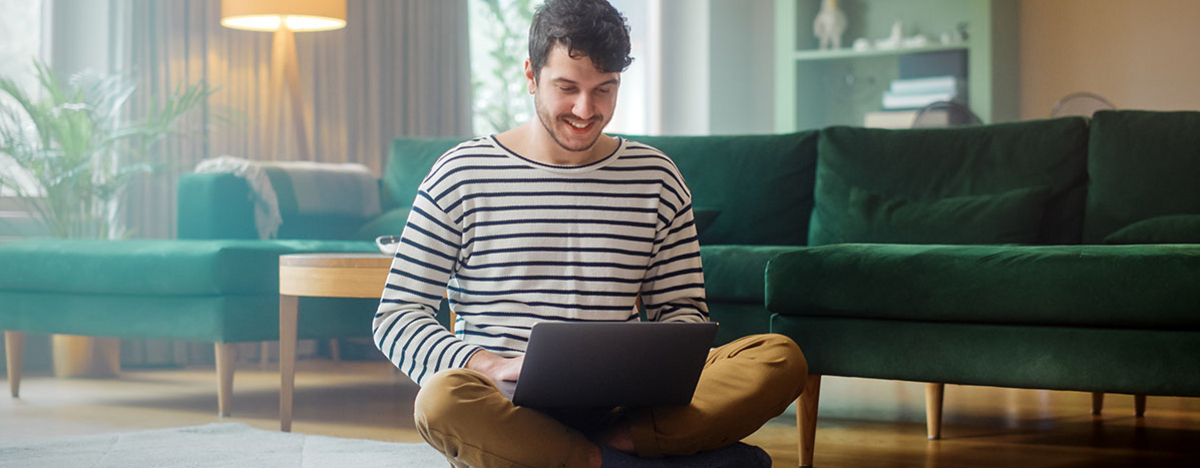 Mann mit Laptop, w&auml;hrend er auf dem Wohnzimmerboden sitzt