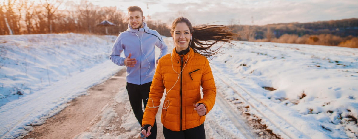 Ein fittes Paar treibt im Winter Sport im Schnee drau&szlig;en und l&auml;uft auf einer verschneiten Stra&szlig;e.
