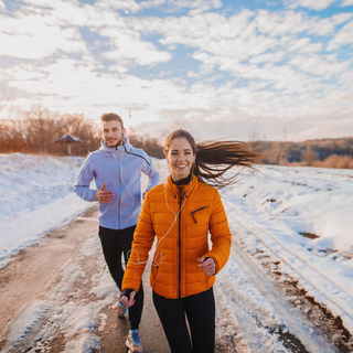 Ein fittes Paar treibt im Winter Sport im Schnee drau&szlig;en und l&auml;uft auf einer verschneiten Stra&szlig;e.