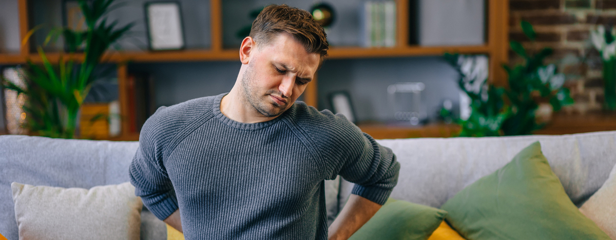 Mann sitzt auf der Couch und h&auml;lt sich den R&uuml;cken