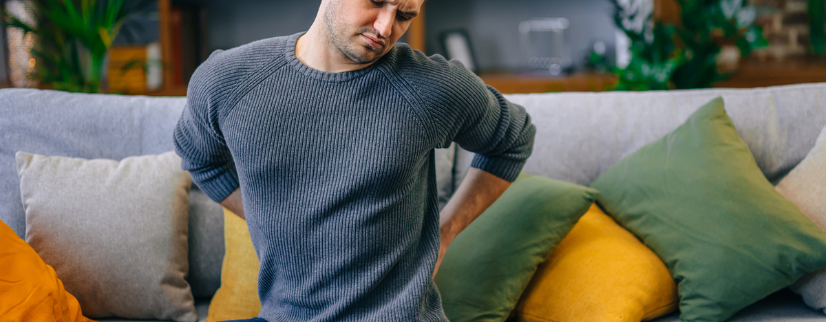 Mann sitzt auf der Couch und h&auml;lt sich den R&uuml;cken