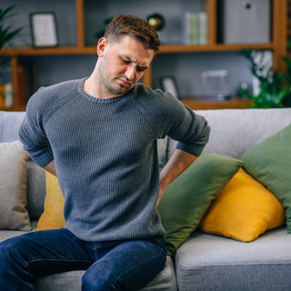Mann sitzt auf der Couch und h&auml;lt sich den R&uuml;cken