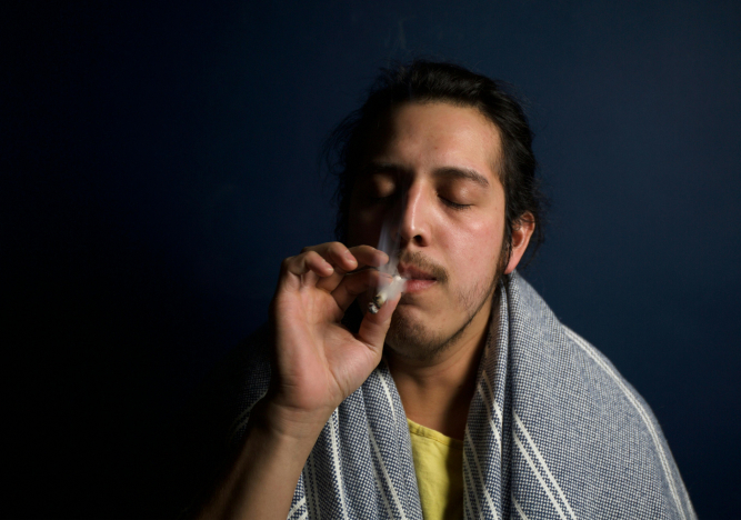 Ein junger Mann mit einem Handtuch um den Hals raucht einen Joint.