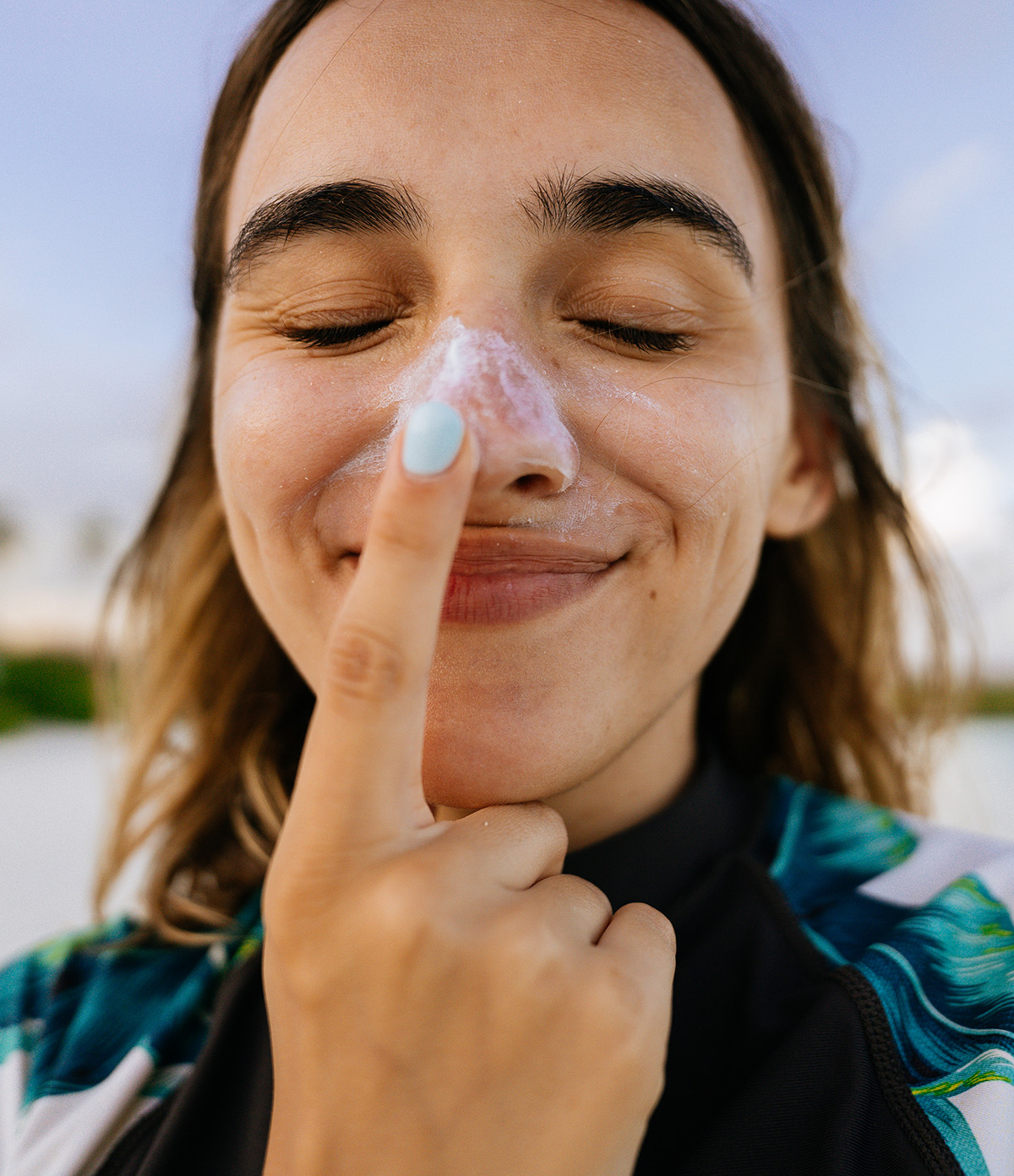 Junge Frau tr&auml;gt Sonnencreme auf ihre Nase auf
