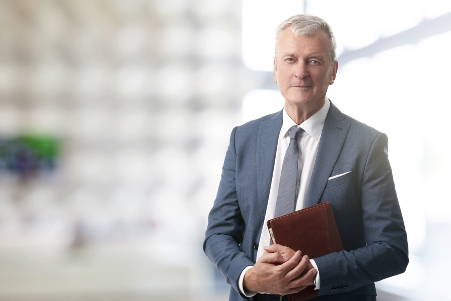 Mann im Anzug steht mit verschr&auml;nkten Armen da und blickt in die Kamera