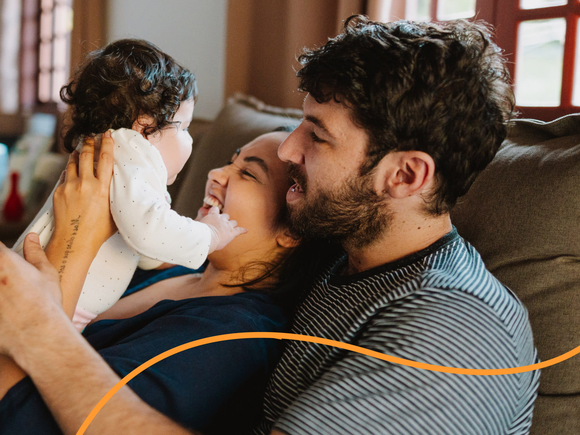Eine junge Familie mit Baby sitzt auf dem Sofa und l&auml;chelt.