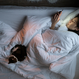 Eine junge Frau liegt im Bett, starrt auf ihr Smartphone und kann nicht schlafen