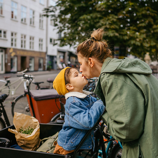 Mutter und Sohn geben sich ein K&uuml;sschen, w&auml;hrend sie bei einem Fahrradst&auml;nder stehen