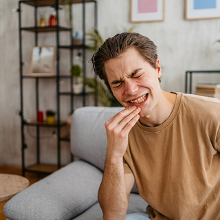 Ein junger Mann mit schmerzverzerrtem Gesicht h&auml;lt sich den Mund.