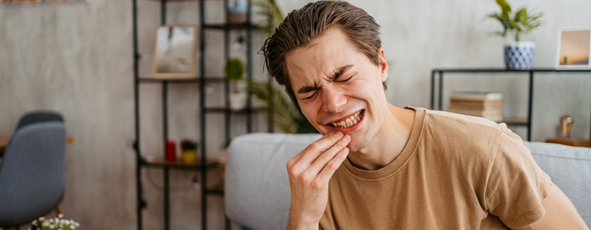 Ein junger Mann mit schmerzverzerrtem Gesicht h&auml;lt sich den Mund.